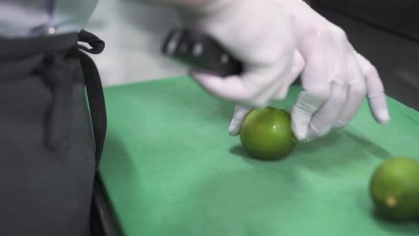 Pracownik w lateksowych rękawiczkach tnie wapno nożem na zielonej desce — Wideo stockowe