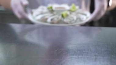 İnsan, lezzetli istiridyelerle dolu tabağı metal tezgahın üstüne koyar.