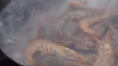 Mutfakta gaz sobasında buhar bulutunda kraliyet karideslerini pişirmek.