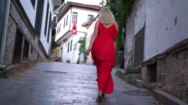 Красива жінка з білявим волоссям у червоній сукні ходить босоніж — стокове відео