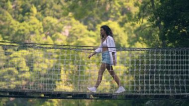 Uzun kıvırcık saçlı esmer asma köprü boyunca yürüyor.