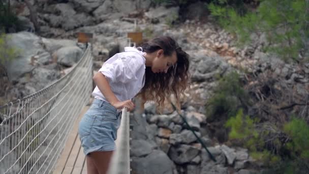 Брюнетка с длинными вьющимися волосами стоит на подвесном мосту — стоковое видео