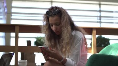 Beyaz elbiseli kıvırcık saçlı kadın akıllı telefondan sosyal ağlar kuruyor.