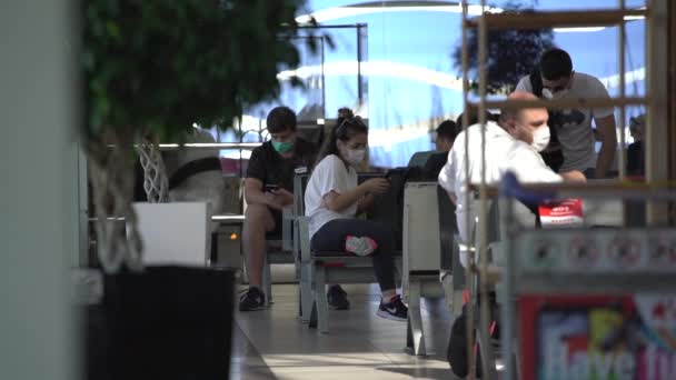 Verschillende mensen in gezichtsmaskers zitten op stoelen in de luchthaven hal — Stockvideo