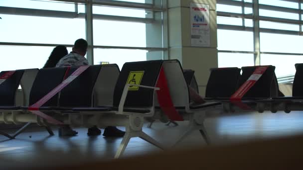 Люди сидят на стульях в зале ожидания аэропорта на социальной дистанции — стоковое видео