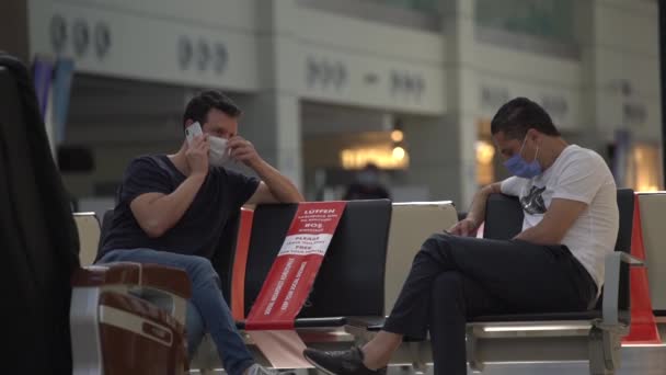 Jongens in wegwerpmaskers zitten met telefoons op terminalstoelen. — Stockvideo