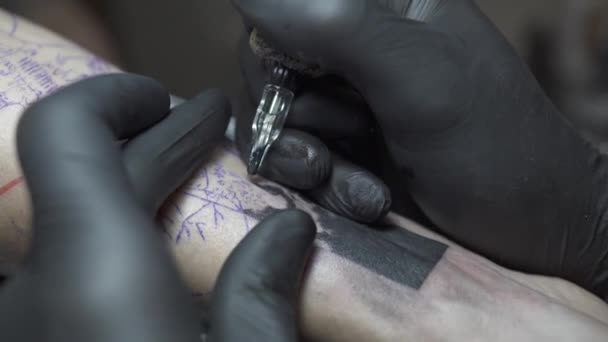 Татуировщик в перчатках создает черное изображение на руке посетителя — стоковое видео