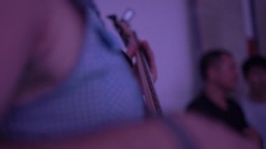 Koyu renk gece kulübünde kolsuz gömlek giyen sanatçı gitar çalıyor.