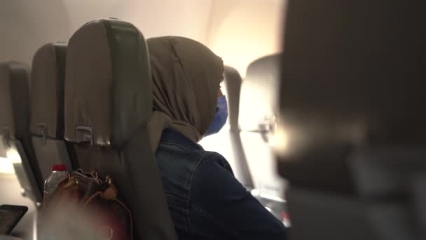 Muselman kvinna i mask och hijab sitter på stol i flygplan — Stockvideo