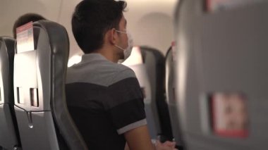 Koruyucu maskeli bir adam uçağın kabininde sandalyede oturur.