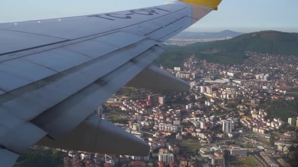 Wing of passenger plane flying above city in clear sky — Stock Video