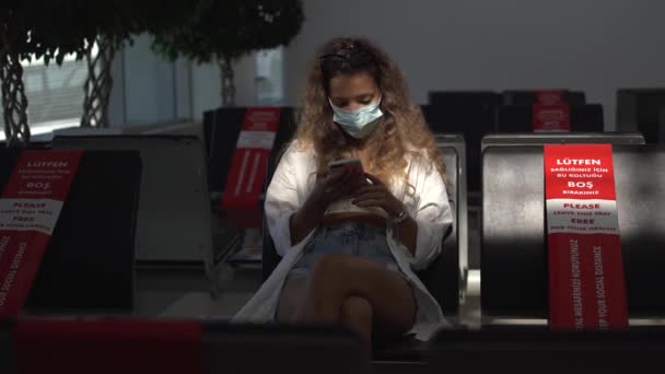 戴面具的妇女坐在机场的椅子上使用手机 — 图库视频影像