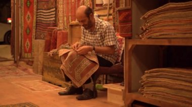 Kel adam dükkanda geleneksel süs eşyalarıyla halı yapıyor.