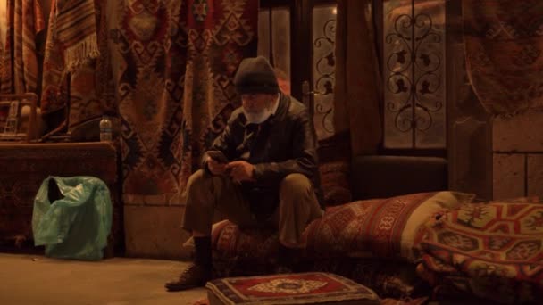 Hombre envejecido con barba gris se sienta en una alfombra grande y se ve — Vídeos de Stock