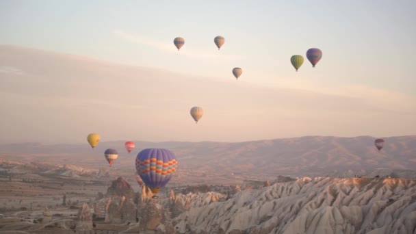 Coloridos globos aerostáticos flotan sobre el paisaje montañoso — Vídeo de stock