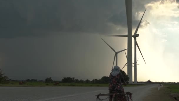 妇女骑着自行车沿着宽阔的柏油路被风车刮着 — 图库视频影像