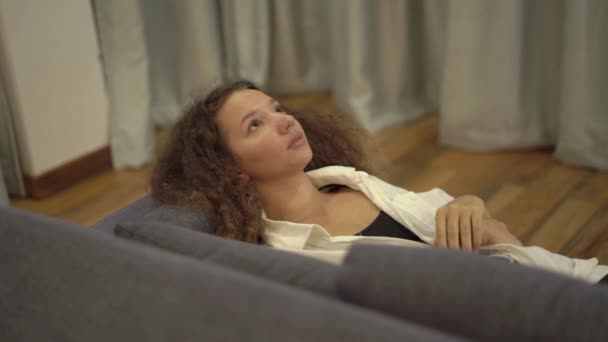 Elegant utmattad dam i svart topp slappnar av på grå soffa — Stockvideo