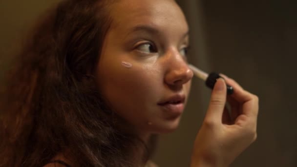 Брюнетка молодая женщина с вьющимися волосами наносит макияж базы — стоковое видео