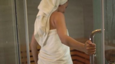 Beyaz havlulu genç bir kadın ev saunasına giriyor.