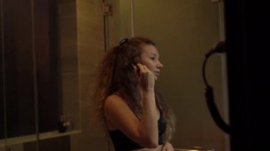 Konsantre bayan banyo aynasına makyaj tozu sürüyor.