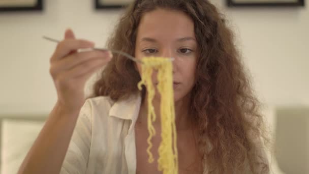 Mujer joven con el pelo rizado suelto come fideos de comida rápida — Vídeos de Stock