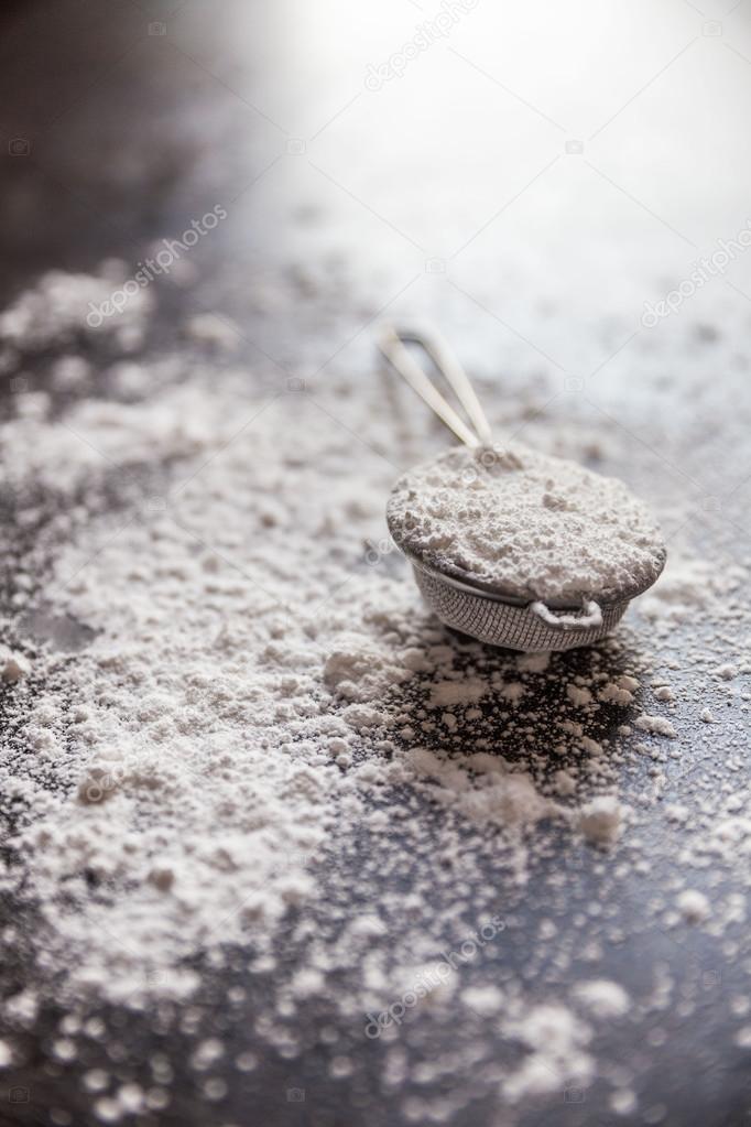 Powdered sugar in a metal strainer on a gray background