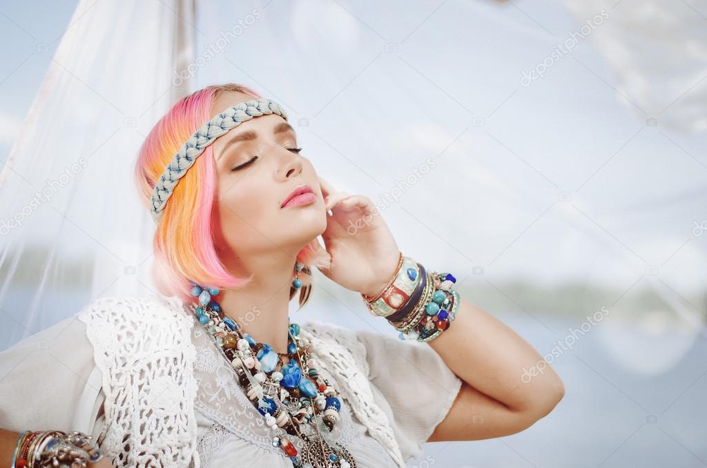 young beautiful girl standing at the summer beach bungalows in bright clothing in the style of boho, with pink hair,with eyes closed