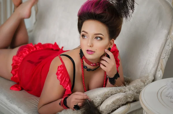 Όμορφο κορίτσι με ένα curvaceous με ροκοκό μαλλιά σε μια κόκκινη ρόμπα ξαπλωμένη στον καναπέ — Φωτογραφία Αρχείου
