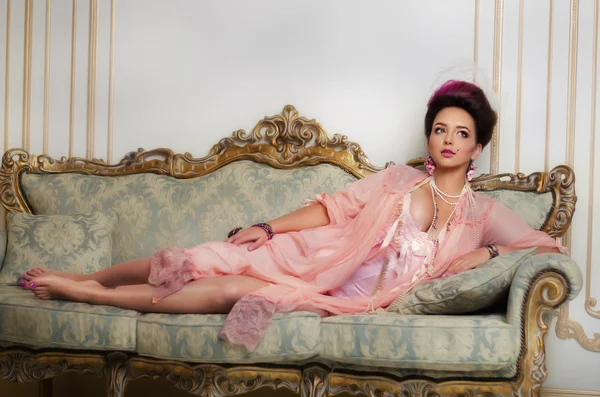 Piękna brunetka z włosami wyprofilowana, rokoko, pierścienie i koraliki polega na kanapie piękny różowy peniuarem — Zdjęcie stockowe