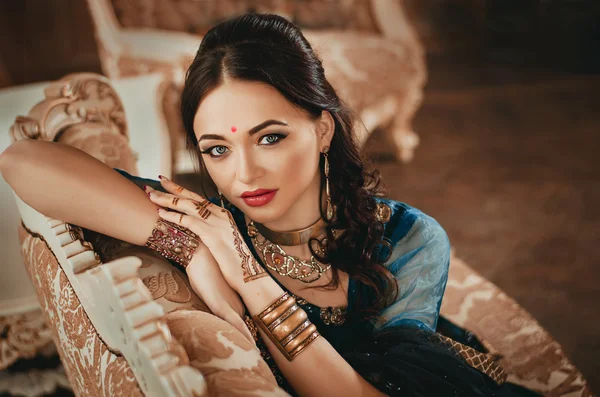 Retrato de uma mulher bonita em vestido chinês tradicional indiano, com as mãos pintadas com henna mehendi. Menina sentada em um sofá de luxo — Fotografia de Stock