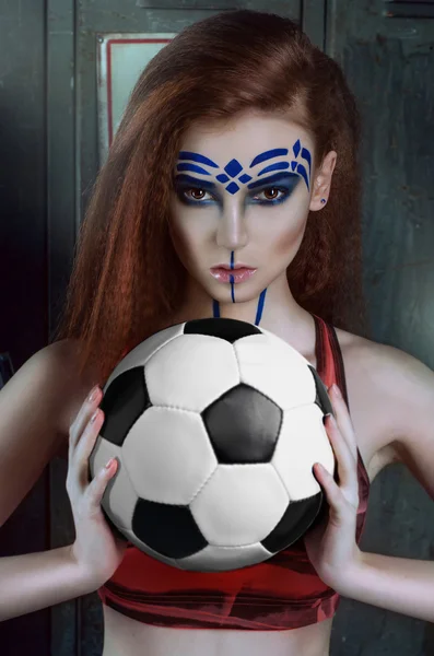 beautiful young woman in a short pink top with a painted face, red hair holding a soccer ball
