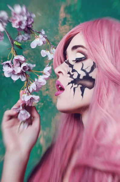 Gyönyörű lány, rózsaszín hosszú haj festett arc gazdaság egy ágacska cherry Blossoms — Stock Fotó