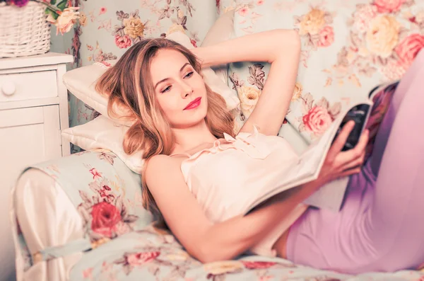 Bela menina deitada no sofá lendo uma revista — Fotografia de Stock