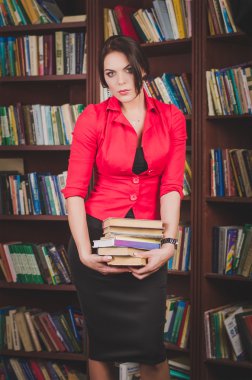 güzel kahverengi saçlı kadın ofis kıyafetleri ayakta raflardan yakınındaki ve kitapların bir yığınına tutar