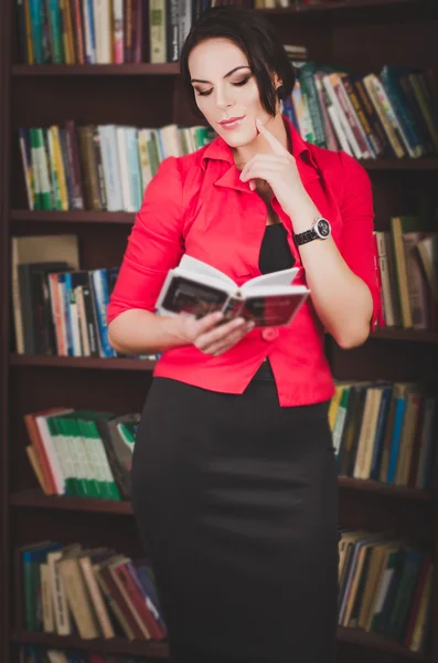 Bella giovane donna dai capelli castani in abito ufficio in piedi vicino librerie — Foto Stock