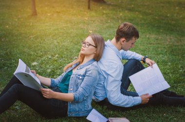 Öğrenciler adam ve kız parkta çim ve r üzerinde oturan