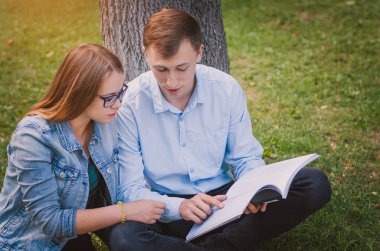 Öğrenciler adam ve kız parkta çim üzerinde oturan ve bir kitap okuma. Eğitim kavramı
