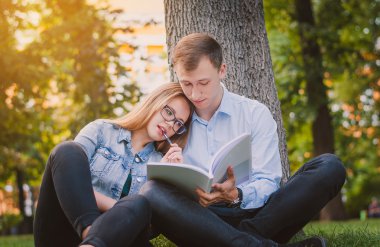 Öğrenciler adam ve kız parkta çim üzerinde oturan ve bir kitap okuma. Eğitim kavramı