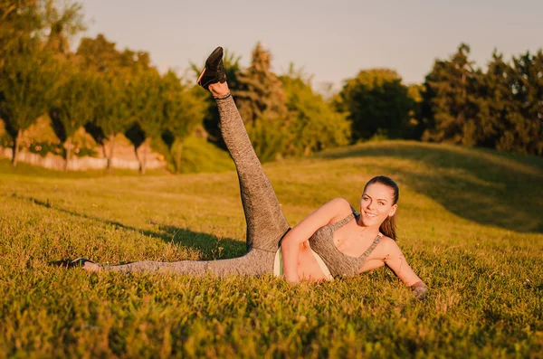 Atractiva mujer de fitness tumbada en el césped en el parque y doin —  Fotos de Stock