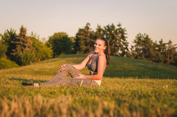 Fitness attraktive junge Frau sitzt auf dem Rasen im Park — Stockfoto