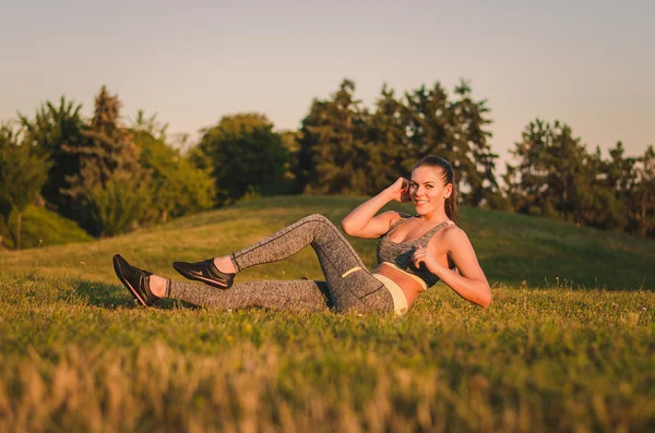 Fitness aantrekkelijke jonge vrouw zittend op het gras in een park doen — Stockfoto