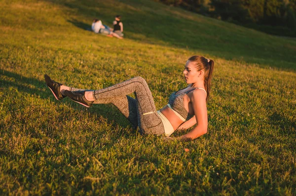 健身有吸引力的年轻女子坐在公园的草地做 — 图库照片