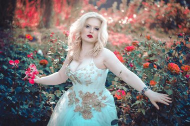 The beautiful blonde with a magnificent forms in the garden among the flowers in a long light dress. Bride on the walk