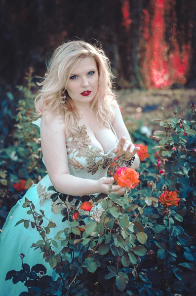 The beautiful blonde with a magnificent forms in the garden among the flowers in a long light dress. Bride on the walk — 스톡 사진