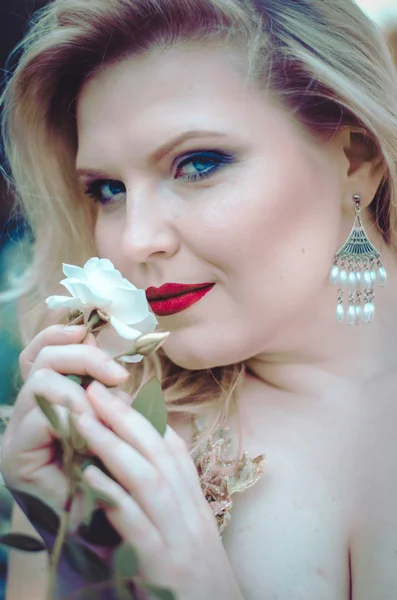 Retrato de uma bela loira com uma forma curvilínea, lábios vermelhos e olhos azuis em um vestido leve em um jardim exuberante entre as rosas. Noiva na caminhada — Fotografia de Stock