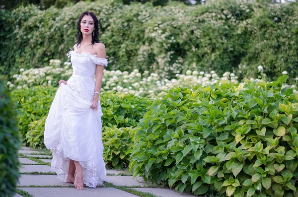 Beautiful young brunette in a white long dress summer garden. Bride on the walk — Stok fotoğraf