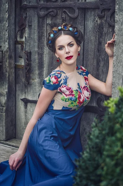 Portrait of a beautiful young brunette in a blue dress, a wreath on his head, blue eyes and red lips against the background of an old wooden door. Deuvshka Ukrainian, Russian girl — Stockfoto