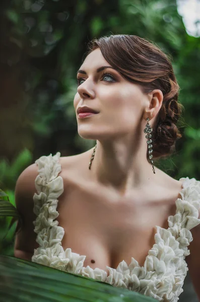 Portrait of a beautiful brunette with blue eyes, white dress and ornaments in the jungle — Stock Photo, Image