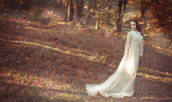 Beautiful young girl in a long gentle waving bright dress stands in the autumn forest. Bride on a walk.