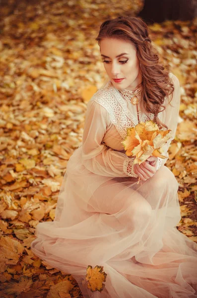 Beautiful young girl with and braided hair and a bouquet of autumn leaves in the hands, a gentle long dress — Stock Fotó